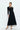 Front view of black twist front stretch knit midi dress with gold hardware