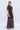 Side view of chocolate brown ruched mesh maxi dress with draped cape detail