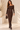 Front view of chocolate brown off shoulder ribbed knit maxi dress with crossed neckline, long sleeves and gold buttons